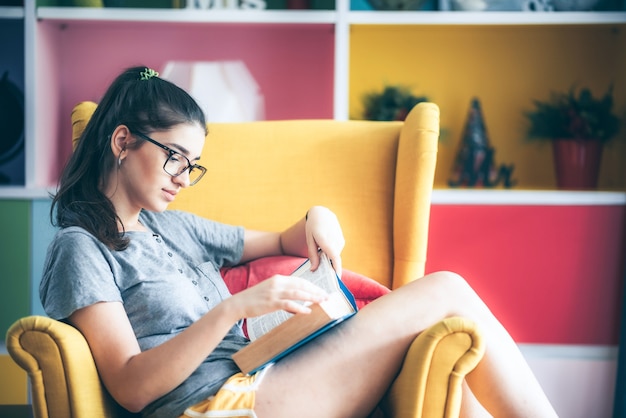 Young women is reading a book text literature on yellow sofa in living room at house, young lady wearing glasses while reading novel, lifestyle concept, relax and enjoy herself, home  isolate