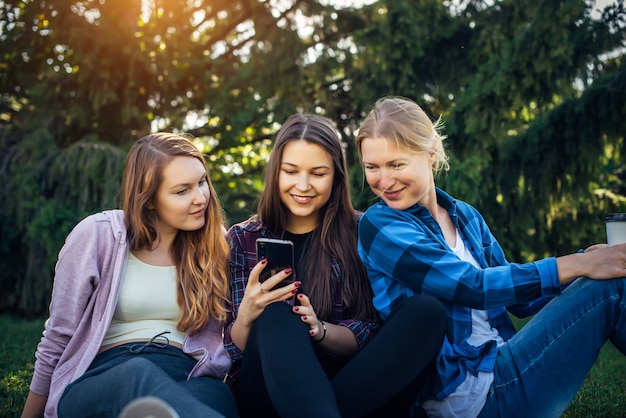 Young women sit on the green grass and look at the smartphone