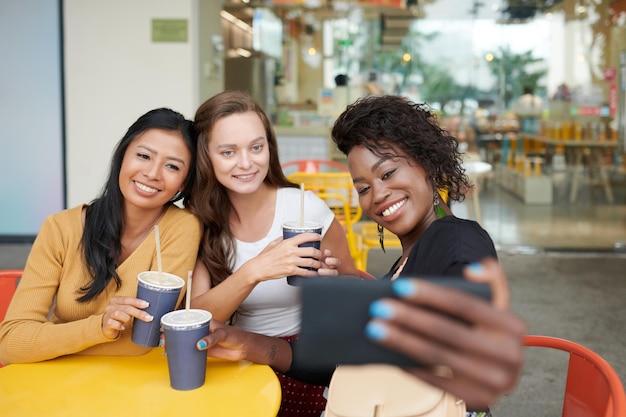 Young women spending time in cafe drinking cocktails and taking photos