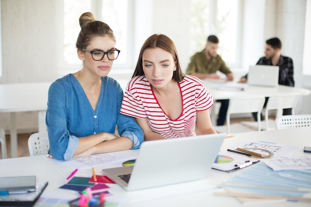 Young women thoughtfully working together with laptop while spending time in modern office