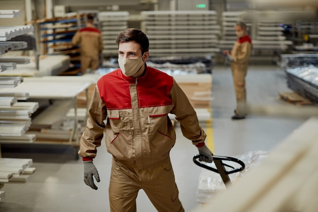 Young worker pulling pallet jack while working at carpentry warehouse