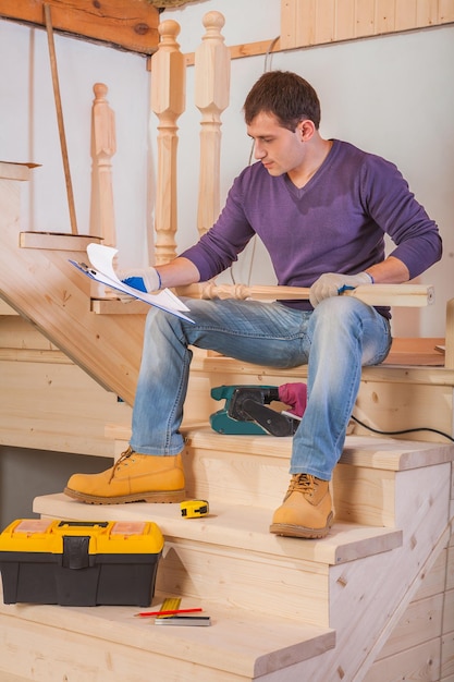 Young worker sitting on wooden ladder and loking in blueprint