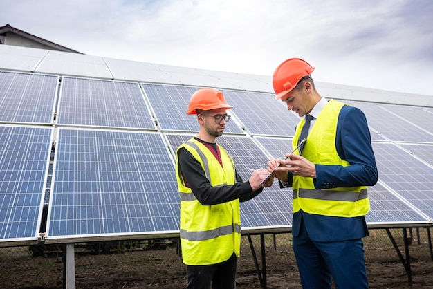 Young workers in helmets of working jackets discuss the plan of work solar panels for economy