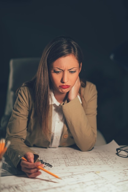 Young worried female architect analyzing blueprint in the office.