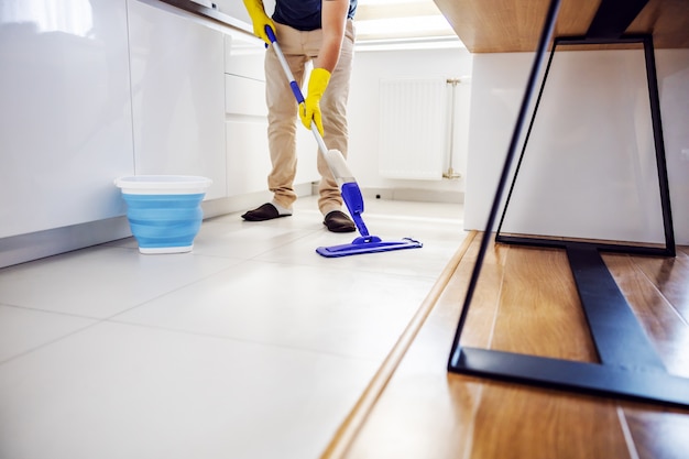 Young worthy man cleaning kitchen floor and trying out new cleaning product.