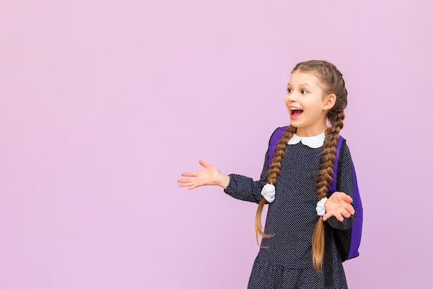 A young young schoolgirl in a polka dot dress and with long pigtails is very happy and smiling