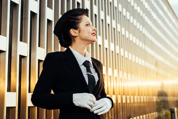 A young young stewardess woman in uniform looks up at the sky and waits for her flight