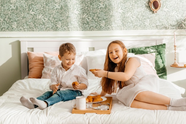 Younger brother and sister have breakfast at home on the bed