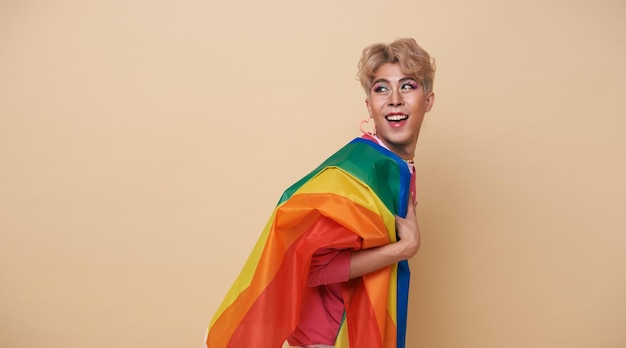 Youth asian transgender LGBT with Rainbow flag on shoulder isolated over nude color background Man with a gay pride flag concept