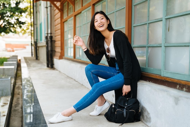 Youth happiness style and clothing concept. Beautiful asian hipster girl with short hair relax sit outdoor. woman leaning on wooden window of old house in tokyo japan looking aside with happy smile.