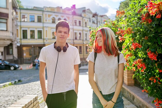 Youth, teenagers, lifestyle, portrait of smiling happy teenage boy and girl college students with backpacks, headphones in sunny city on the street