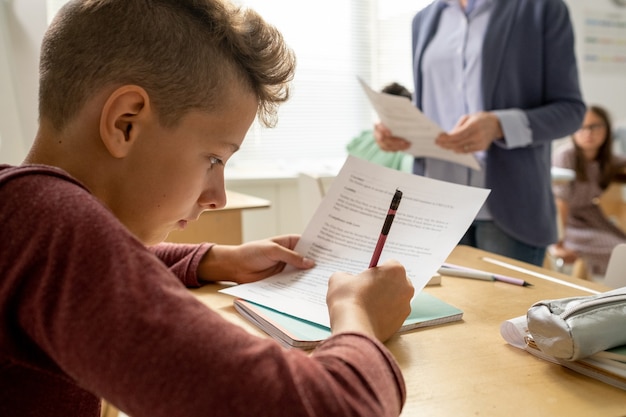 Youthful schoolboy carrying out test by desk