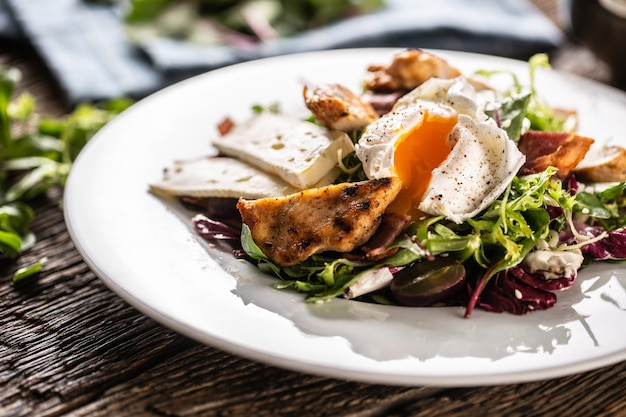 Yummy fresh summer like lettuce salad made of various types of leafs served on the plate with pieces of delicious sheep cheese, grilled crunchy chicken breasts and seasoned runny egg.