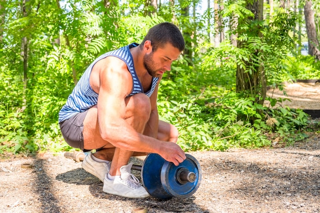 Yyoung athletic man puts weights on the barbell for outdoor exercise