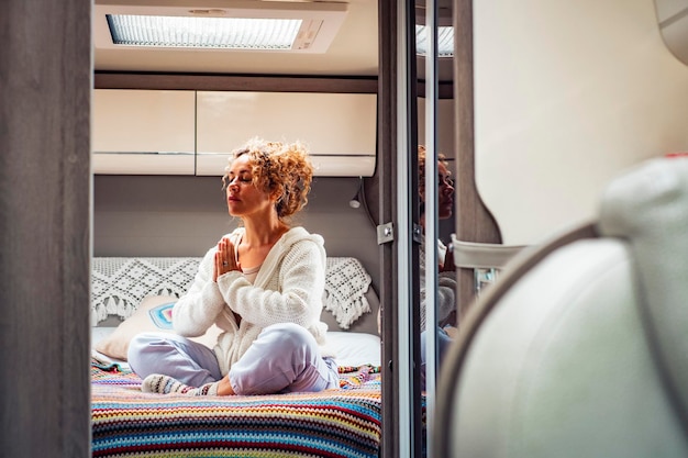 Zen and meditation indoor leisure activity One woman in yoga relax loto position sitting inside a bedroom of modern camper van Alternative and travel lifestyle Inner balance and love female people