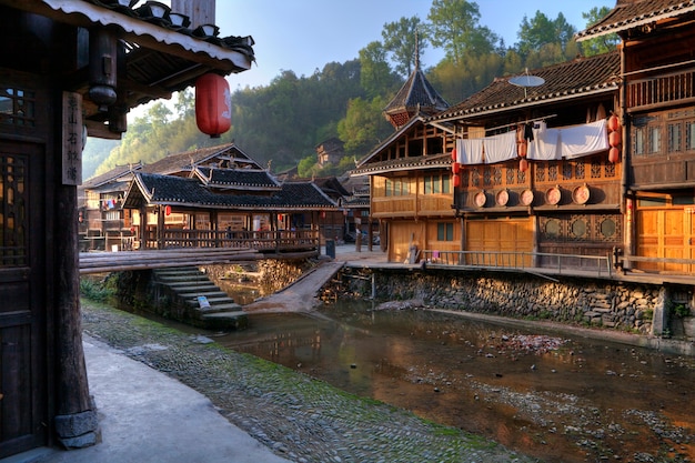 Zhaoxing Dong Village, Guizhou Province, ethnic minorities in southwest China in  light of sunset, wooden house and  covered bridge over countryside river.