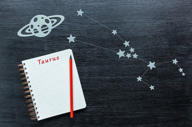 Zodiacal star, constellations Taurus on a black background with a notepad and pencil.