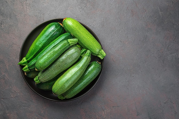 Zucchini in a black plate on a gray-brown background. Top view, copy space.