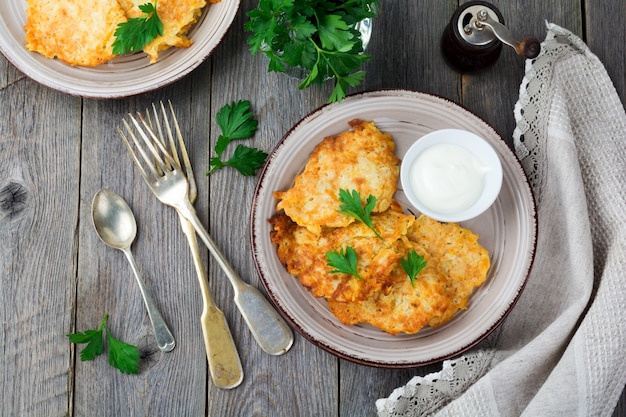 Zucchini fritters, homemade vegetarian zucchini pancakes with fresh herbs and yogurt sauce on a white ceramic plate on old wooden table. Rustic style. Selective focus. Top view. Place for text.