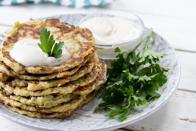 Zucchini fritters with yogurt sauce on white wooden table