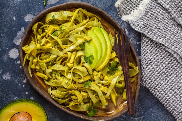 Zucchini pasta with pesto and avocado in dark dish. Healthy vegan food.