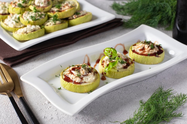 Zucchini slices baked with feta cheese and garlic served with balsamic on a white plate on a light gray background