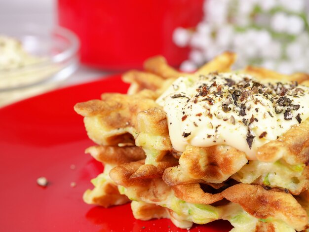 Zucchini waffles on a red plate with sauce and spices