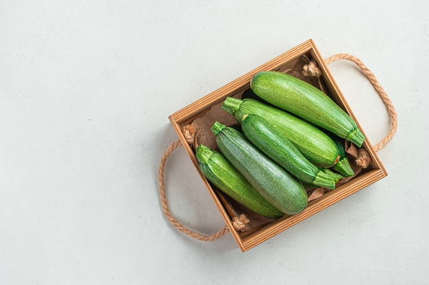 Zucchini in a wooden box on a gray background. Top view, copy space.