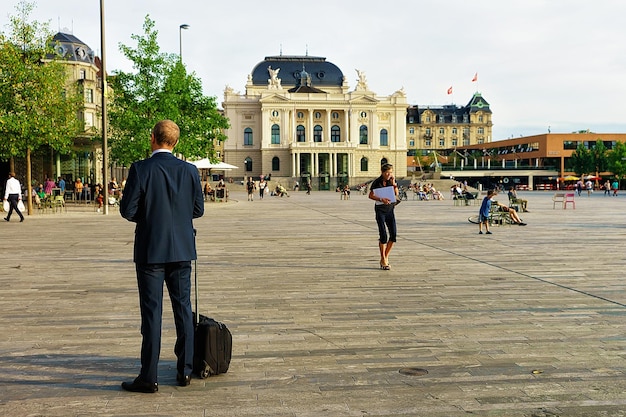 Zurich, Switzerland - September 2, 2016: Man with luggage on Sechselautenplatz at Opera House in Zurich old city center, Switzerland. People on the background