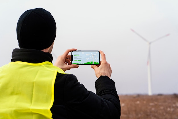 PSD back view of male engineer photographing wind turbine in the field