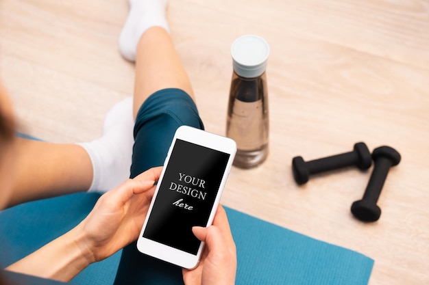 Back view of sportive woman resting on the floor using modern smartphone Mockup