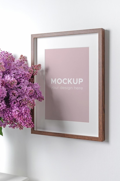 Blank vertical frame mockup on white wall with lilac flowers