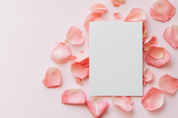 Blank vertical invitation or greeting card mockup with light pink background and pink rose petals