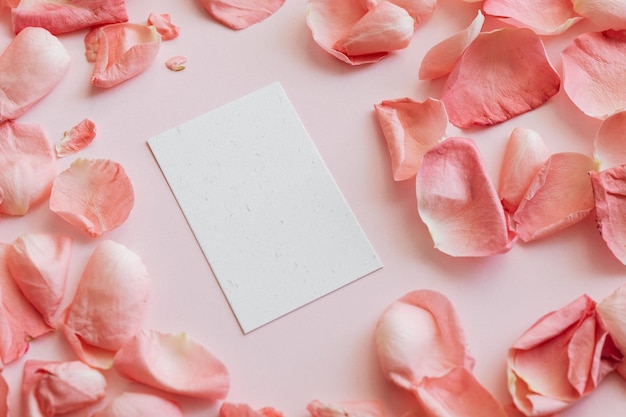 Blank vertical invitation or greeting card mockup with light pink background and pink rose petals