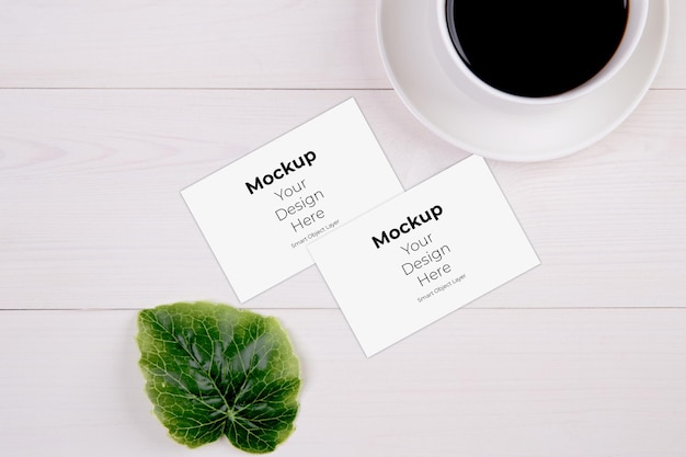 Business card mockup with leaf and cup of coffee on wooden table