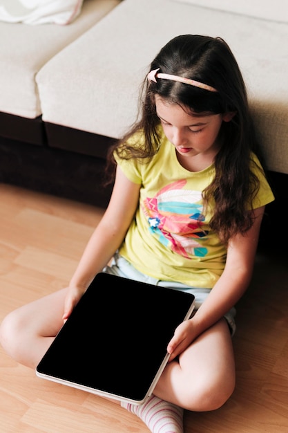 Child sitting on a floor with a digital tablet in her hands