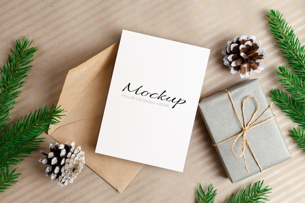 Christmas greeting card mockup with envelope, gift box and fir branches and cones decorations