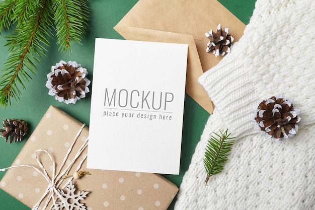 Christmas greeting card mockup with gift box, fir tree branches with cones on knitted background