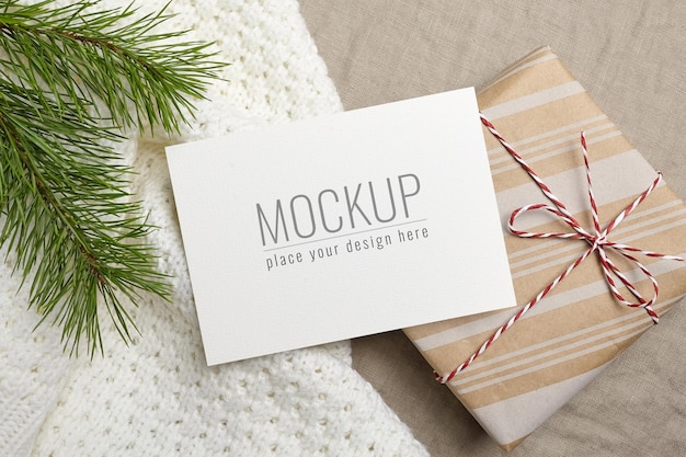 Christmas greeting card mockup with gift box and pine tree branch on knitted background