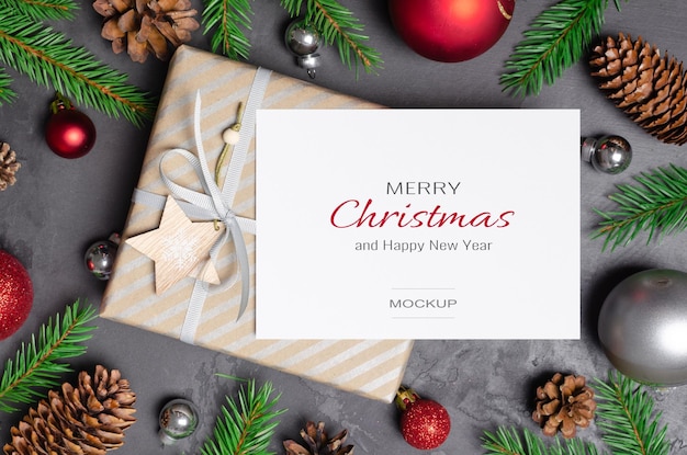 Christmas greeting card mockup with gift festive decorations fir tree twigs and cones on dark background