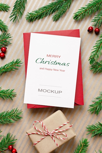 Christmas greeting card mockup with red envelope, gift box and decorated fir tree branches