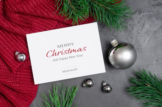 Christmas greeting card mockup with silver festive decorations and pine tree branches on red knitted background