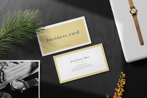 Clean minimal business card mockup on black table background with paper conifer plant and watch on box