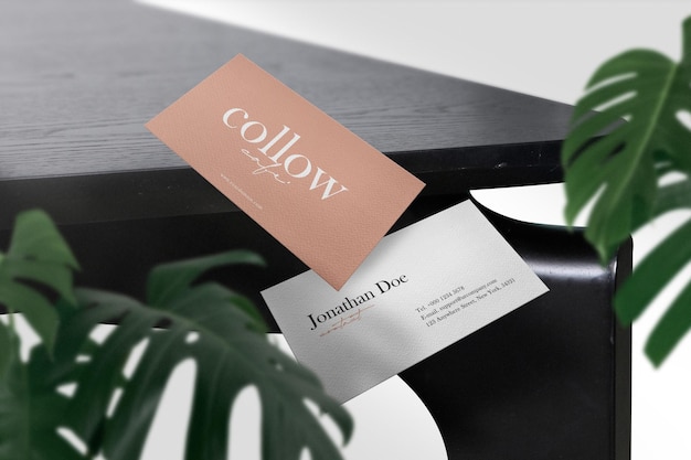 Clean minimal business card mockup on black table with green leaves 