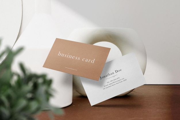 Clean minimal business card mockup floating on the top wooden with white earthenware and leaves background. PSD file.