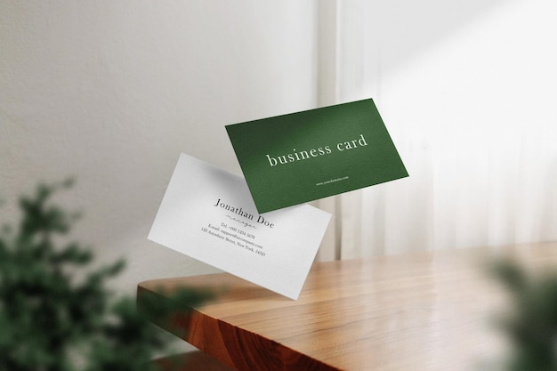 Clean minimal business card mockup floating on wiiden table with plant background PSD file