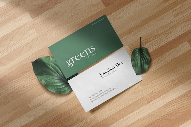 Clean minimal business card mockup on wood floor with green leaves