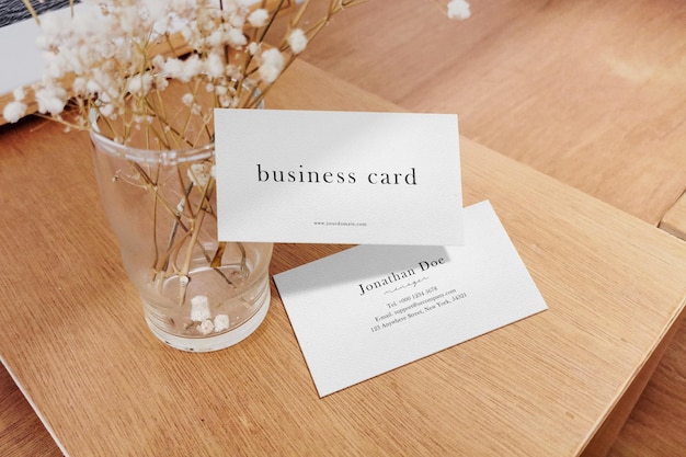 Clean minimal business card mockup on wooden plate with glass vase and dry flower background. PSD file.