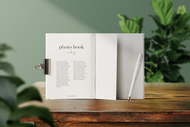 Clean minimal paper book opening mockup standing on wooden top with pen and plant background PSD file