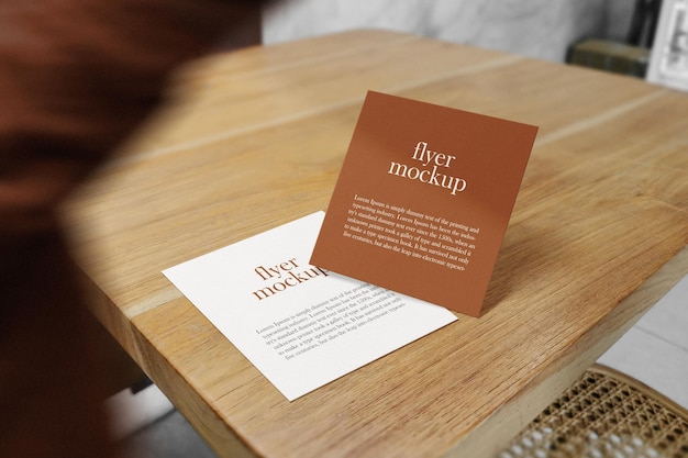 Clean minimal square flyer mockup on wooden top table with people walking blur foreground